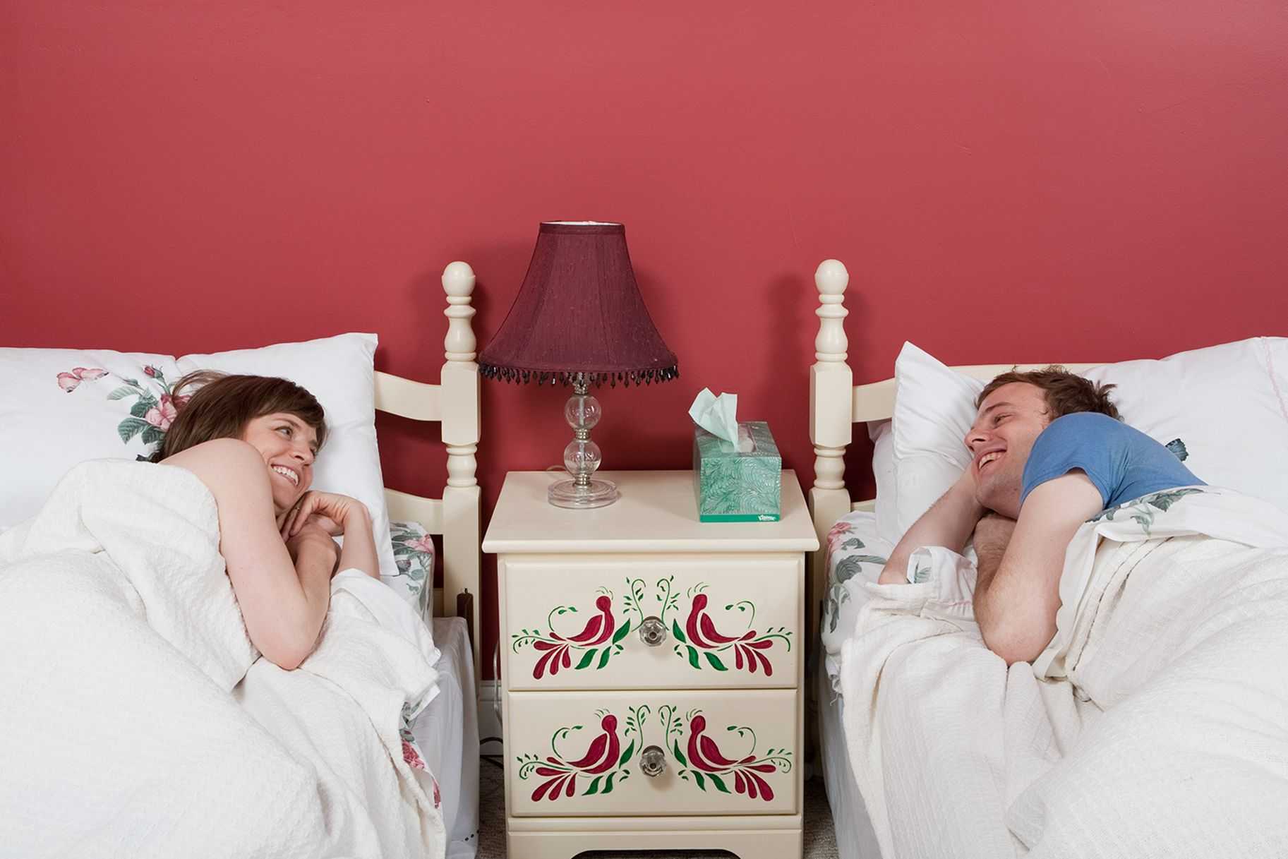Жена укладывает мужу спать. Фотосессия в спальне. Сон супругов. Спят в разных комнатах. Отдельные кровати для супругов.